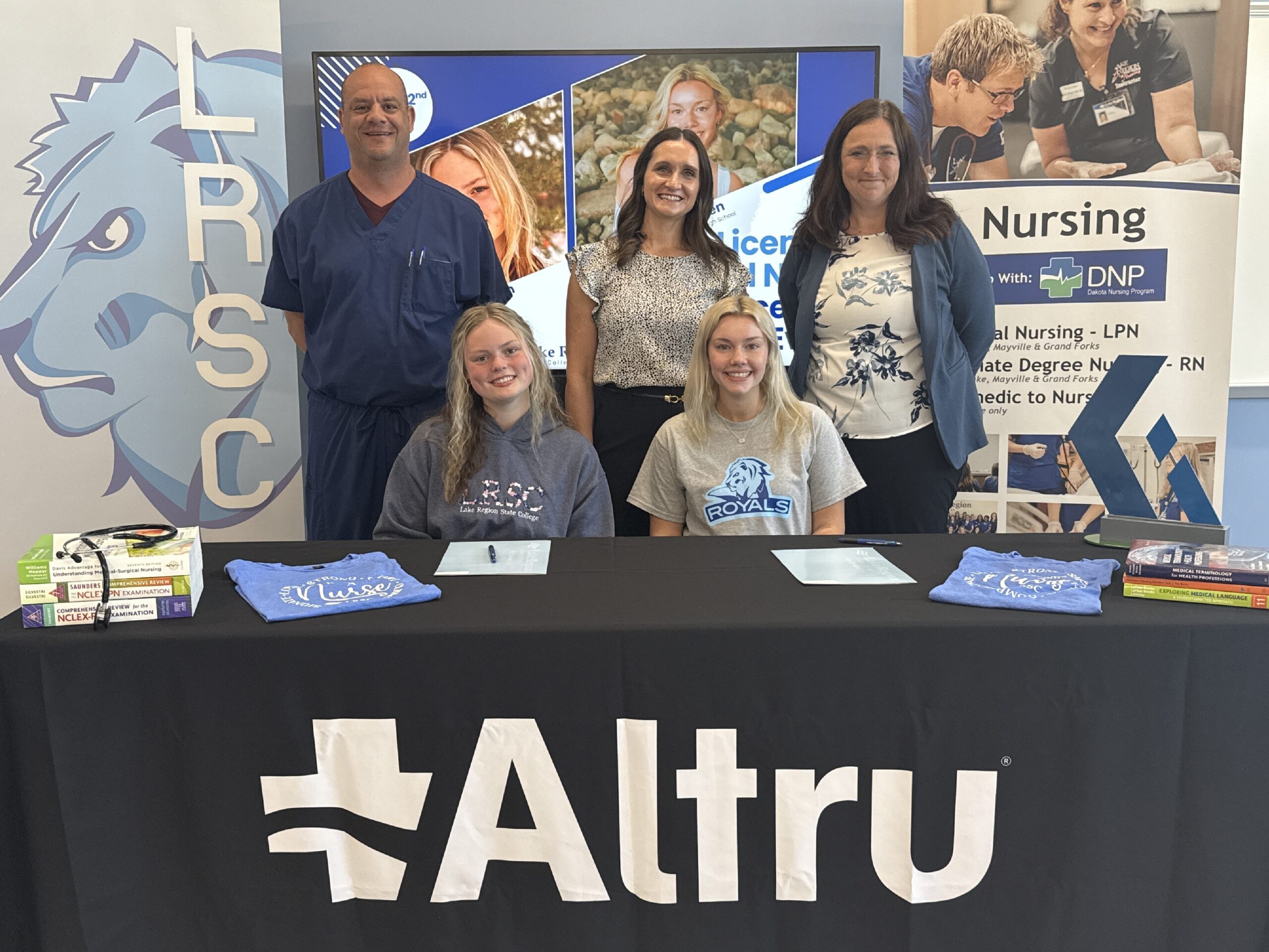 Two new nursing apprentices pose at an Altru table with three people involved with the program