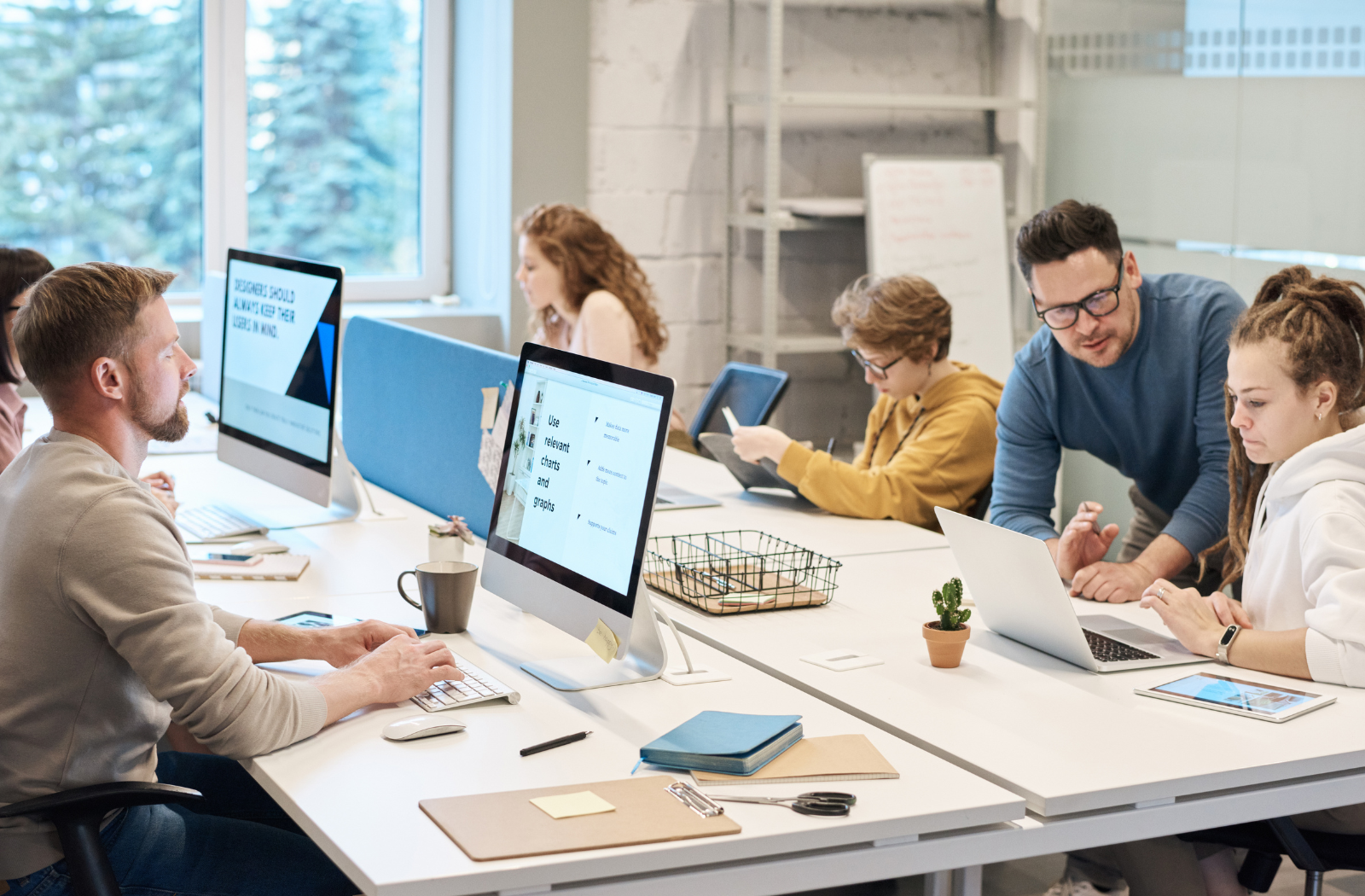 A group of employees work on computers at a long table