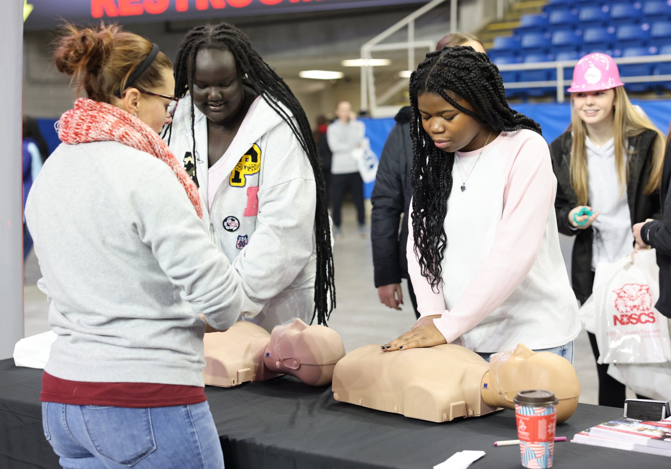 Two students at a career fair meet with a health professional at a booth featuring CPR training