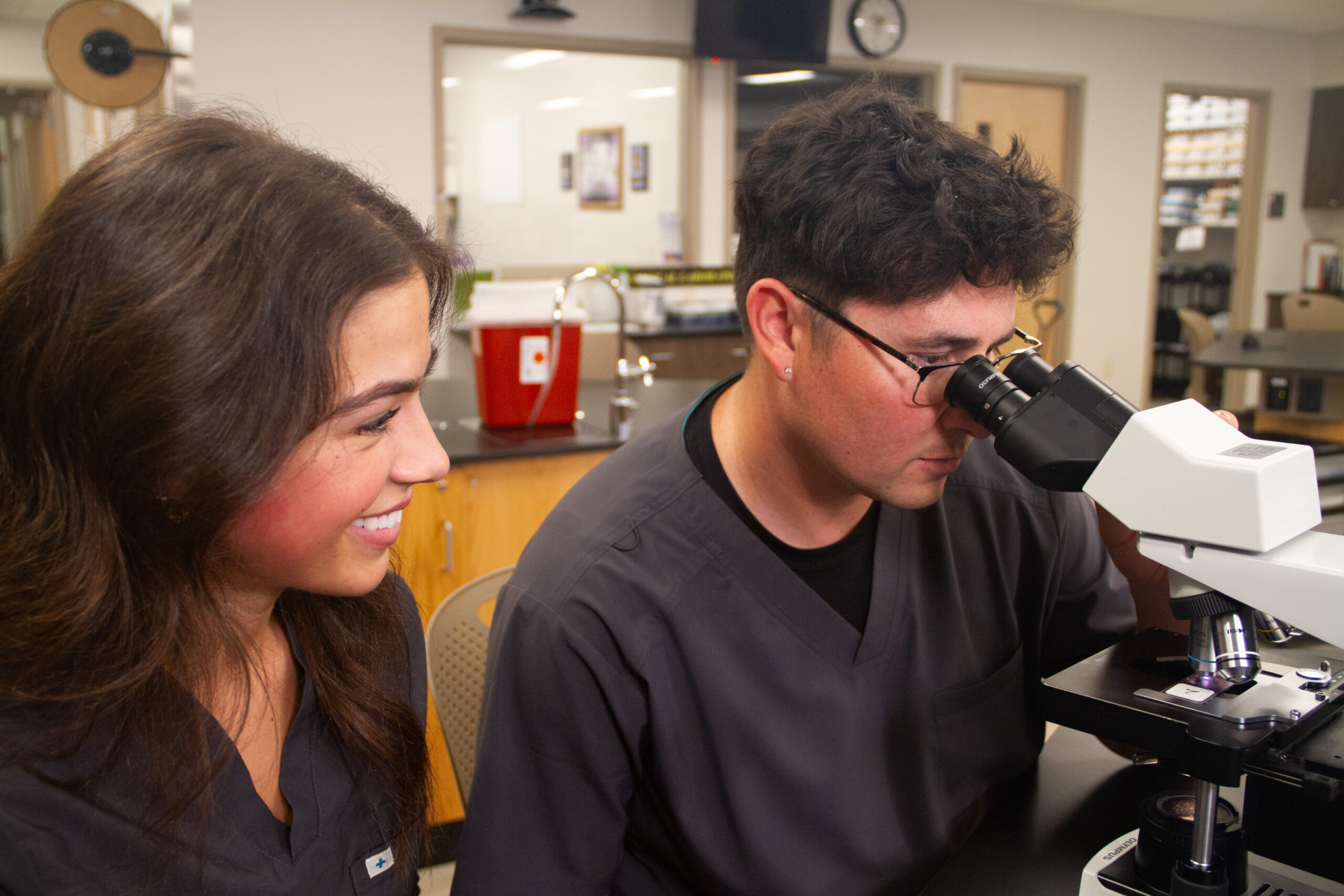 Two medical lab technician students work at a microscope together